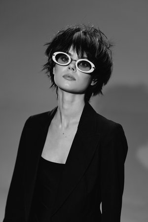 Stylish woman wearing white round sunglasses and black outfit in black and white portrait with short...