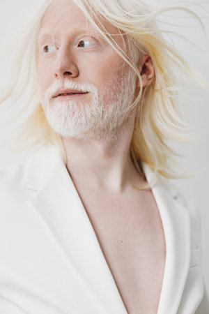 Portrait of an elegant individual with long light hair and a beard, set against a soft white background, conveying beauty and uniqueness with a striking and ethereal presenceの写真素材
