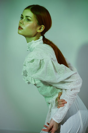 Elegant model with long red hair in a vintage white blouse against a green toned background, expressing serene beauty and calmness in a minimalist styleの写真素材