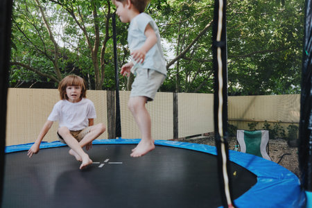 Active boys playing on a trampoline, enjoying the outdoors with laughter and joy. This engaging scene captures the essence of childhood excitement and fun.の写真素材
