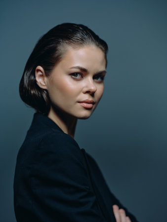 Portrait of confident young woman with short hair wearing dark clothing on blue background, poised and thoughtful expressionの写真素材