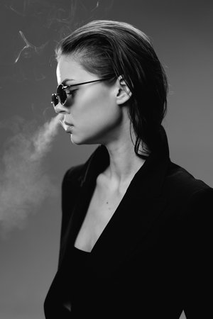 Black and white portrait of a young woman wearing sunglasses with smoke silhouette, stylish and mysterious mood.の写真素材