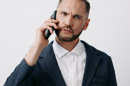 A business professional man speaks on a mobile phone, expressing intensity and focus, set against an...