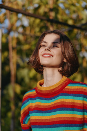 Young woman striped sweater smiling outdoors sunlight bob haircut casual outfit autumn joyful, standing in a sunlit garden looking up peacefully for lifestyle and fashion portrait.の写真素材