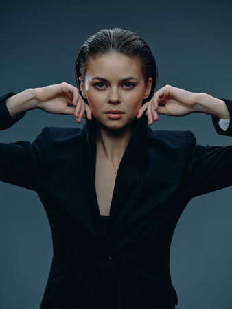 Confident woman in black blazer posing with hands near face, wet hair, serious expression, studio background, stylish portraitの写真素材