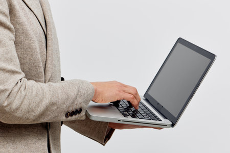 man working with laptop in beige jacket typing on keyboard isolated plain background digital nomad...