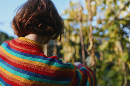 Woman in striped sweater seen from back view in a garden outdoors, short hair, casual outfit, reaching among plants, relaxed lifestyle scene for fashion and travel imagery.の写真素材