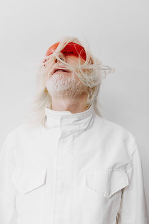 Fashionable elder man with long white hair wearing striking red sunglasses, against a minimalistic white background, exuding a sense of modernity and uniquenessの写真素材