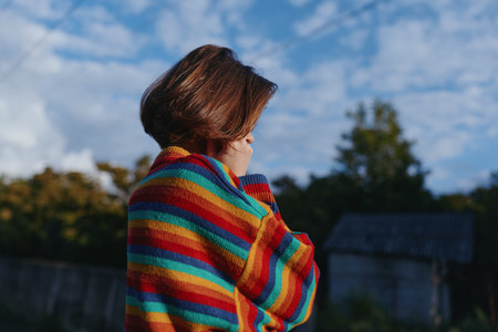 Woman in a colorful striped sweater with short hair outdoors, looking down in a contemplative pose....