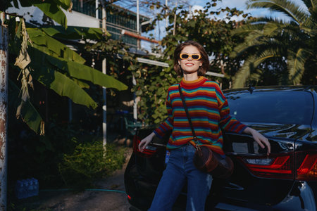 Woman striped sweater sunglasses leaning car tropical smiling casual outfit with crossbody bag and...