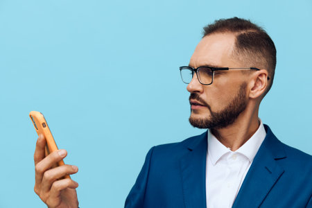 A professional business man in a sharp blue suit checks his smartphone, displaying focused and confident emotions against a solid color background.の写真素材