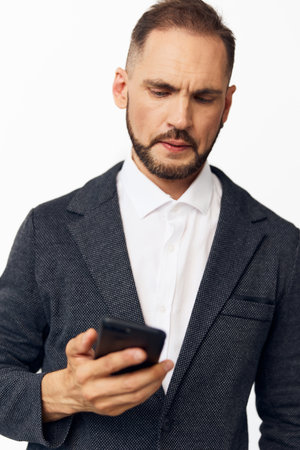 A professional man in business attire studies a mobile device against an isolated colored backdrop, showcasing focus, determination, and thoughtful mood in a clean corporate scene.の写真素材