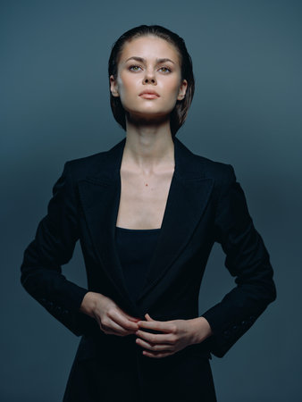 confident woman in black blazer with serious expression on gray backgroundの写真素材