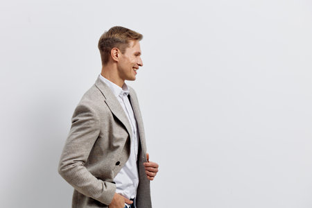 Professional portrait of a smiling young man wearing a gray checkered blazer and white shirt, standing in profile against a plain white background. Studio shot showcasing confident and friendly expression, suitable for business or lifestyle use.の写真素材