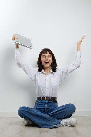 Joyful person sits on the floor in casual attire, raising a notebook with excitement. A bright studio setting conveys energy, creativity, and positive learning vibes.の写真素材