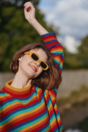 woman smile sunglasses rainbow sweater portrait happy fashion outdoors young adult with short hair raising arm enjoying sunny day in colorful knit jumper and joyful relaxed expressionの写真素材