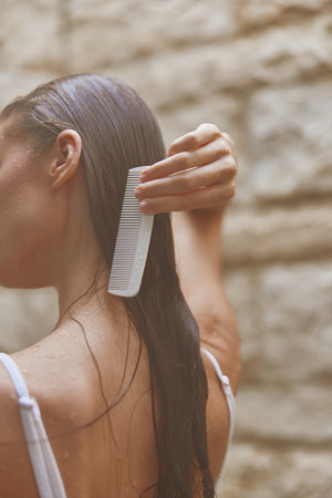 woman combing wet hair with white comb, close-up, natural light, soft focus, healthy hair care, serene momentの写真素材