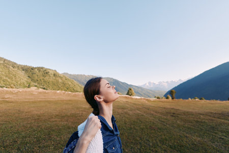 Woman with backpack in mountain meadow enjoying fresh air and nature, hiking and travel portrait with closed eyes, peaceful scenic landscape and relaxed outdoor adventure.の写真素材