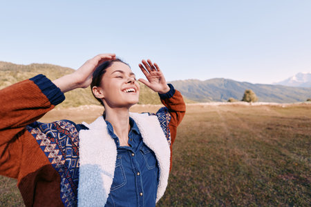 Woman smiling with eyes closed outdoors in countryside, hands raised enjoying nature and warm...