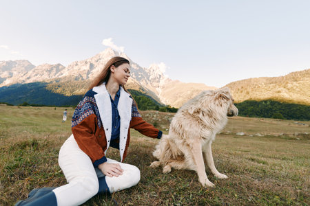 Woman petting a dog in a mountain meadow, outdoor portrait of pet and owner sitting on grass, smiling and enjoying nature in a cozy sweater, relaxed friendship moment.の写真素材