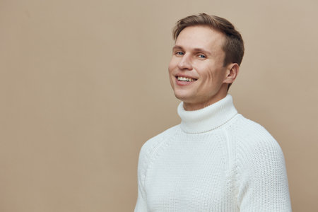 Smiling man wearing white turtleneck sweater looking at camera isolated on beige background studio portrait. People lifestyle conceptの写真素材