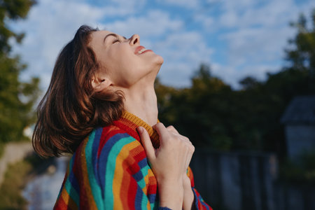 Woman smiling looking up in a colorful striped sweater, outdoor portrait of a joyful casual 30s...