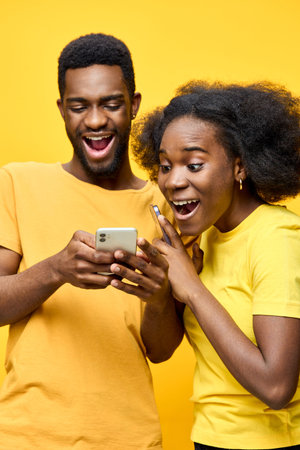 Joyful young couple celebrating a surprise on a smartphone, vibrant yellow background, conveying happiness and connectionの写真素材