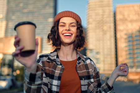 Woman with coffee and bright smile in urban portrait wearing beanie, city morning sunlight and golden glow, candid lifestyle frame conveying authenticity, mindful living and emotional storytelling.の写真素材