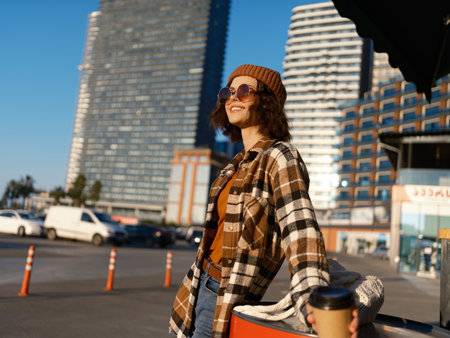 Woman in urban street holding coffee, candid portrait capturing authenticity and golden hour glow, warm smile and mindful lifestyle vibe with relaxed fashion and modern mood.の写真素材
