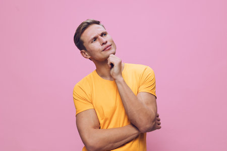 thoughtful man wearing yellow t-shirt looking up pink background mental health and gadgets concept...