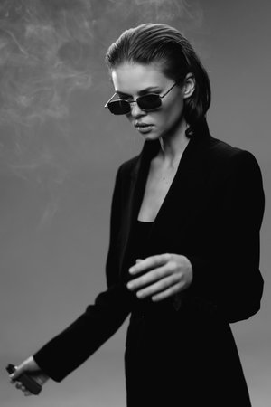 Stylish woman in sunglasses and black jacket with smoky background, confident pose, monochrome portrait, elegant fashion mood.の写真素材