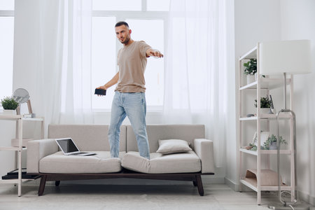 A creative man confidently expressing freedom while balancing on a couch, showcasing a modern lifestyle filled with energy and inspiration in a bright, minimalistic room.の写真素材