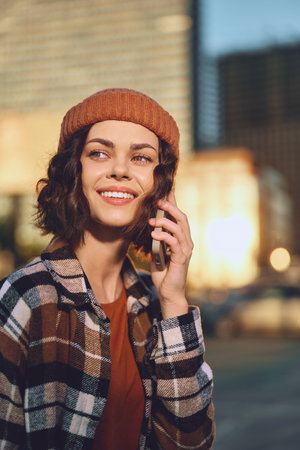 Woman smiling on phone in urban portrait during golden hour glow, candid lifestyle and authenticity captured with beanie, warm sunlight and emotional storytelling for mindful living.の写真素材