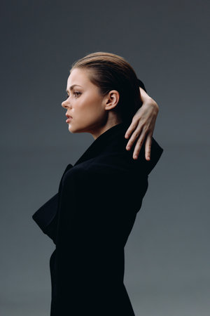 Elegant woman in black coat with thoughtful expression on gray background, minimalistic style, soft lighting, autumn conceptの写真素材