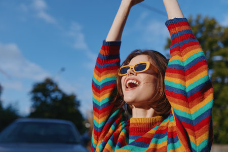 Woman young adult smile in striped sweater and yellow sunglasses outdoor by parked car, joyful arms raised, casual outfit street style, travel and lifestyle vibeの写真素材