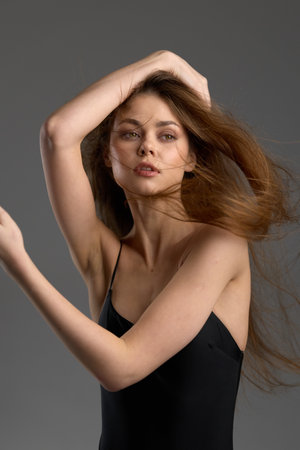 Young woman with long hair posing in black dress with dynamic movement and confident expressionの写真素材