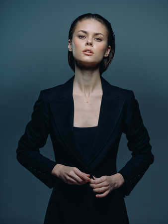Confident woman in black blazer posing with serious expression in a dark studio settingの写真素材