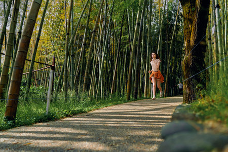 Woman running on gravel path through dense bamboo forest, jogging alone on a scenic trail surrounded by green nature, outdoor fitness exercise and healthy lifestyle and mindful breathing.の写真素材
