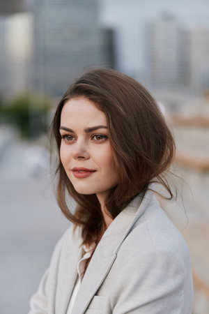 Professional woman in a light gray blazer with natural makeup, exuding confidence against an urban city background, embodying modern business style and ambition.の写真素材