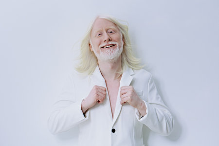 Smiling mature man in a white suit against a plain light background He exudes confidence and joy while holding his blazer Stylish, elegant portrait for fashion and lifestyle themesの写真素材
