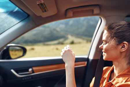 Woman in a car looking out the window during a road trip, enjoying scenic landscape with warm sunlight, relaxed expression and travel vibe in a modern vehicle.の写真素材