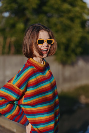 Woman smile portrait outdoors in colorful striped sweater and yellow sunglasses, casual fashion look with short bob hair, joyful expression and warm natural light.の写真素材
