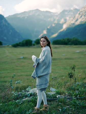 Woman in cozy sweater standing in a mountain meadow, portrait outdoors with scenic landscape and soft light, relaxed pose in leggings and boots, countryside nature and serene atmosphere.の写真素材