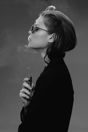 Black and white profile of a stylish woman smoking with glasses and short hair, expressing calm and cool attitude in minimalistic setting.の写真素材
