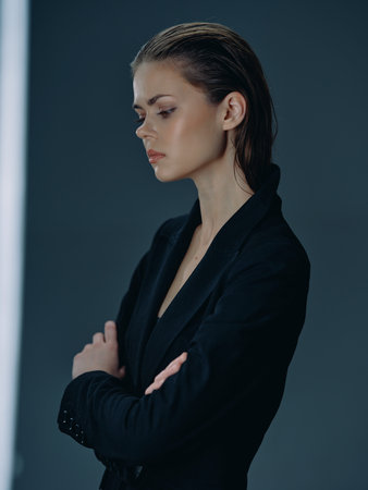Serious woman in black jacket posing with arms crossed against dark background.の写真素材