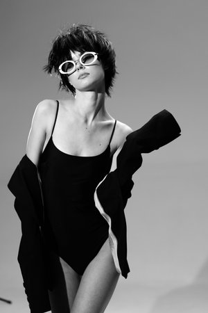 Black and white portrait of a fashionable young woman wearing sunglasses and a swimsuit with a jacket.の写真素材