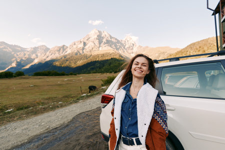 Woman, car, mountains, travel, smile, outdoors, road, adventure: Happy young woman standing by a white SUV on a rural mountain road, smiling during a scenic outdoor road trip with towering peaks.の写真素材