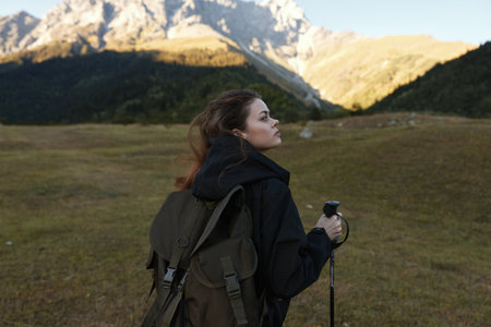 A lone female hiker stands with a backpack in a rugged mountain landscape, gazing toward distant...
