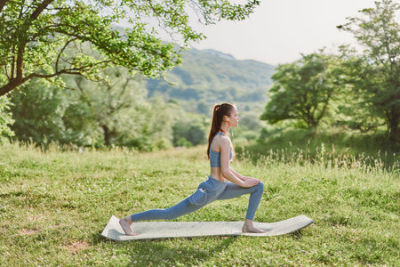 Young woman practicing yoga in a serene natural setting, wearing light blue activewear, showcasing a...