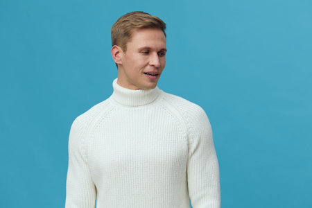 smiling young caucasian man wear white knit sweater look side standing blue background digital detox mental health conceptの写真素材